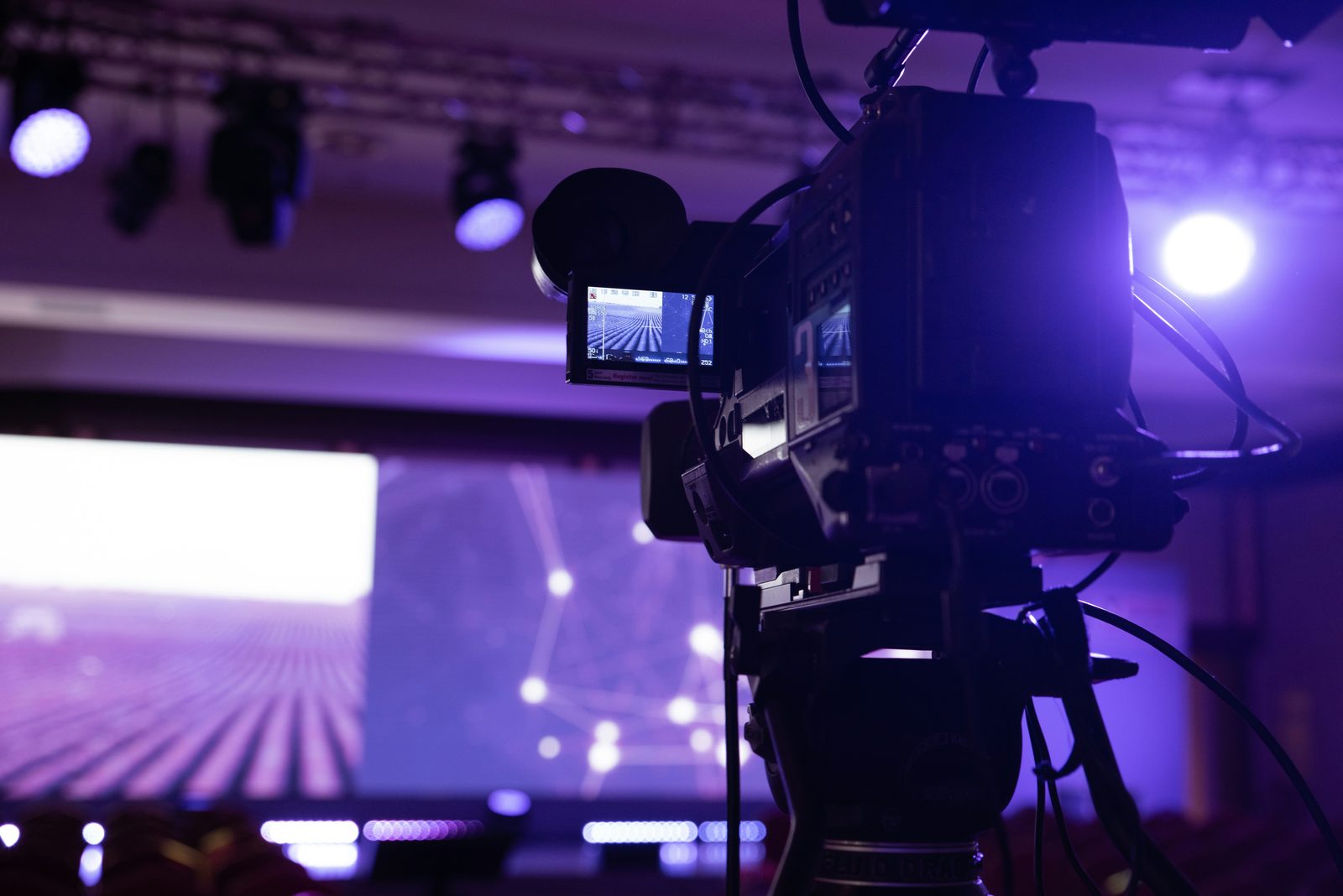 Video camera on a tripod pointed at a lit stage